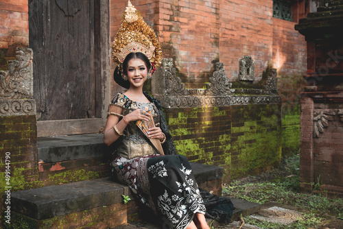 Young Balinese girl in golden headdress sits on the steps of the temple