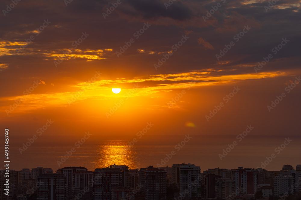 The sun coming out from behind the clouds. Sunset over the city by the sea.