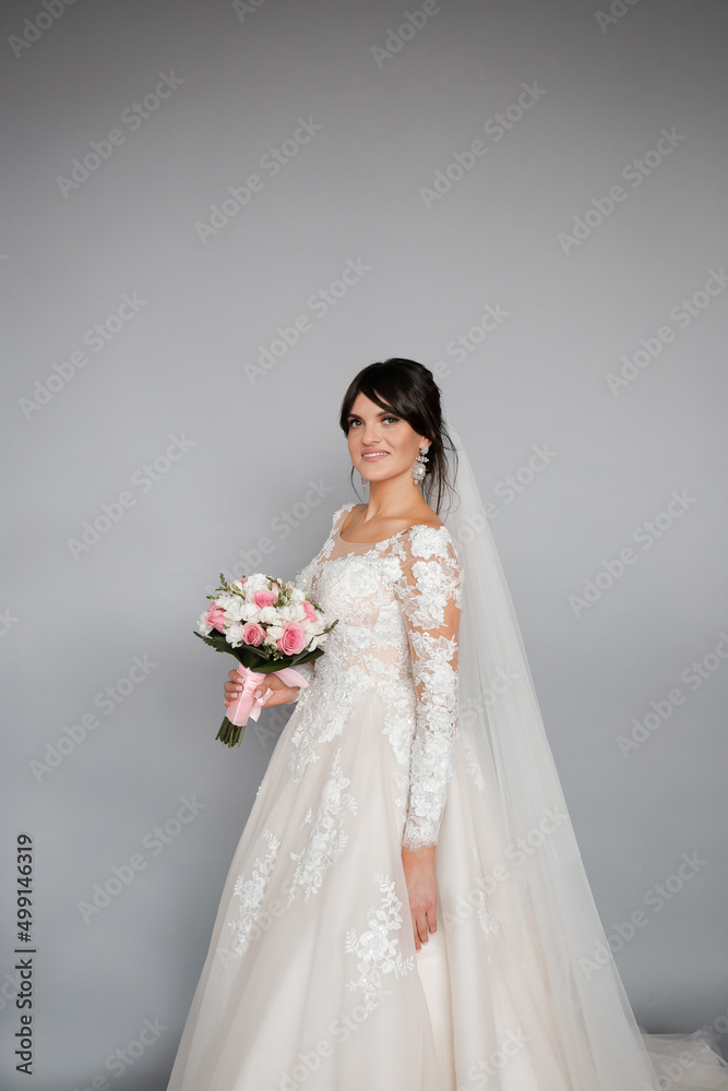 Portrait of the bride. Attractive young girl look at the camera in a white wedding dress and veil holding a bouquet of white and pink flowers in her hands on a background of green trees Portrait of the bride. Attractive young girl look at the camera in a white wedding dress and veil holding a bouquet of white and pink flowers in her hands on a background of green trees