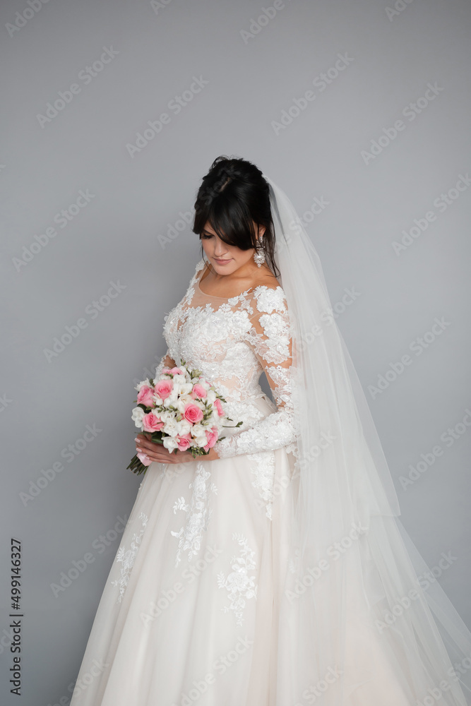 Portrait of the bride. Attractive young girl look at the camera in a white wedding dress and veil holding a bouquet of white and pink flowers in her hands on a background of green trees Portrait of the bride. Attractive young girl look at the camera in a white wedding dress and veil holding a bouquet of white and pink flowers in her hands on a background of green trees