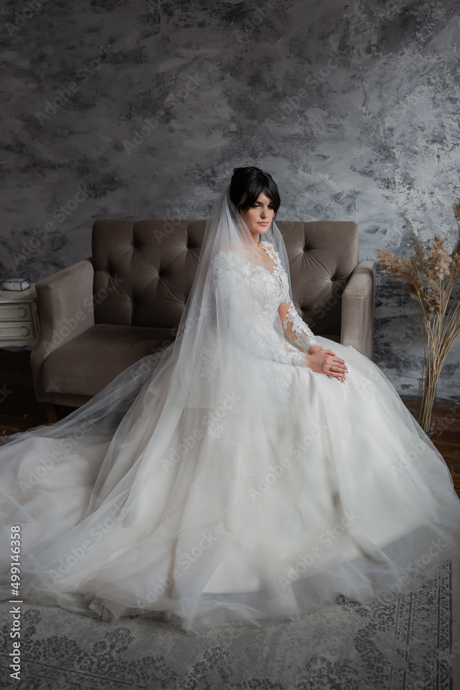 Portrait of the bride. Attractive young girl look at the camera in a white wedding dress and veil holding a bouquet of white and pink flowers in her hands on a background of green trees Portrait of the bride. Attractive young girl look at the camera in a white wedding dress and veil holding a bouquet of white and pink flowers in her hands on a background of green trees