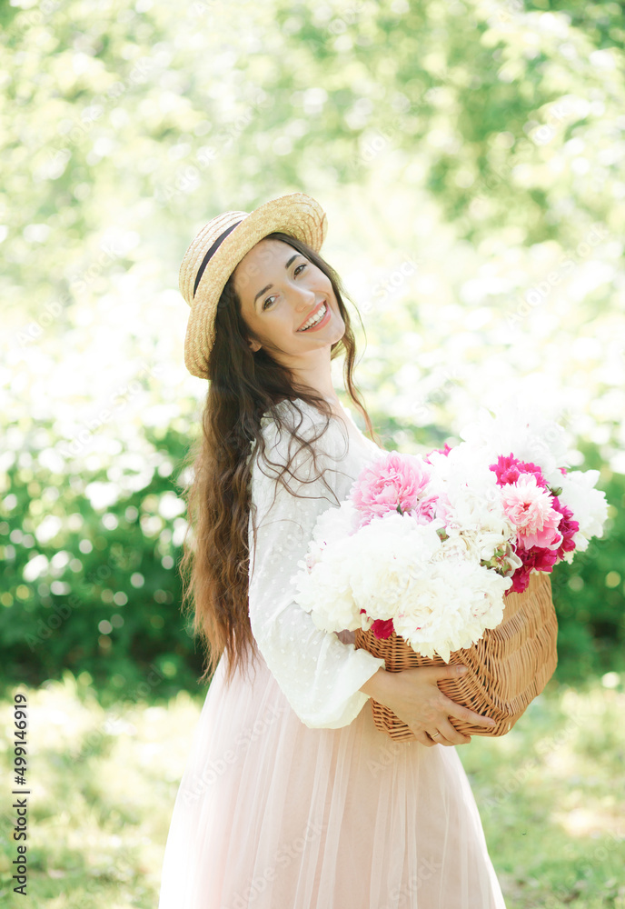 Happy smiling girl in a straw hat holding a wicker basket with white and pink peony flowers posing on the streets of a European city. Lifestyle Happy smiling girl in a straw hat holding a wicker basket with white and pink peony flowers posing on the streets of a European city. Lifestyle