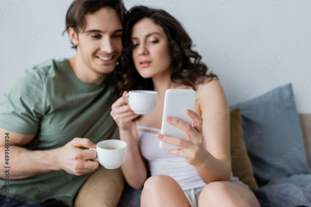 blurred couple with cups looking at smartphone in bedroom. blurred couple with cups looking at smartphone in bedroom.