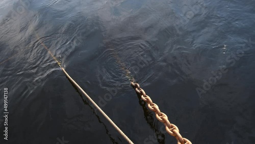Chains and ropes on the pier going under the water, the reflection of the sunset on the waves
