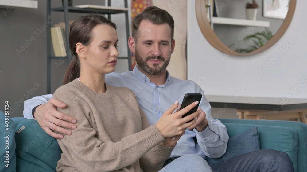 Fototapeta premium Portrait of Couple using Smartphone While Sitting on Sofa