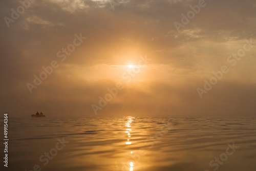 Foggy yellow sunrise. Landscape of morning daun with fishing boat in haze