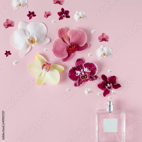 Orchid flowers scent sprayed from perfume bottle with blanc label for copy. Simple square composition on light pastel pink background.