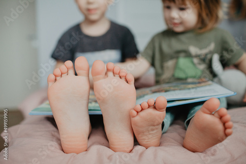 Big brother and little sister holding bare feet close up to camera . Blurred face on background 