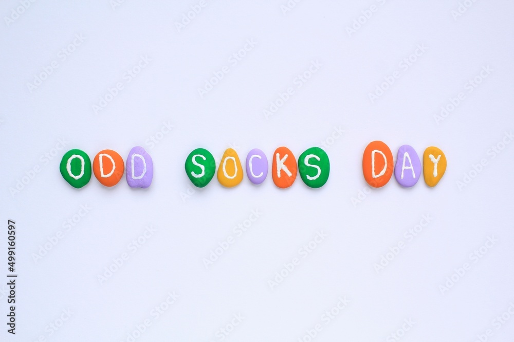 Fototapeta premium Odd socks day lettering on colorful stones pebbles on white background. Social school bullying concept. Lost lonely socks. Top view flatlay idea for poster, banner, advertising