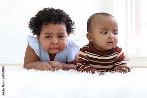 Sad little African American girl with curly hair and baby sister crying, drop of tear running down cheek, eye discharge, kid getting upset and bad-tempered.