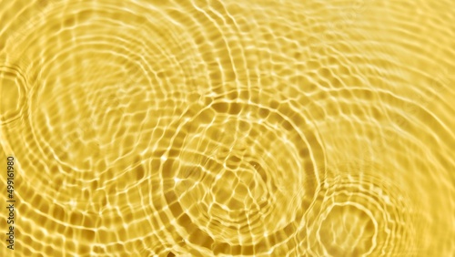 Multiple drops falling on water surface making circles on yellow background | Cosmetics background, skin hydration concept