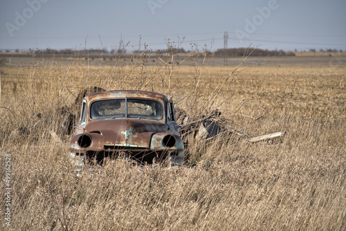 Abandoned classic car sits along a corn field
