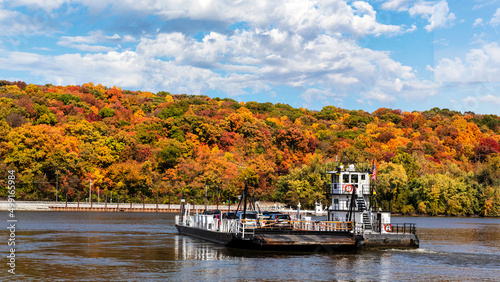 Valokuva A ferry carries cars across the Mississippi River from Missouri to Illinois and autumn rural countryside landscape with trees with colorful fall leaves on a hillside