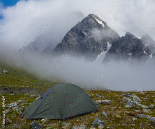 green touristic tent stay on mountain pass in mist and dense clouds, high mountain touristic travel background