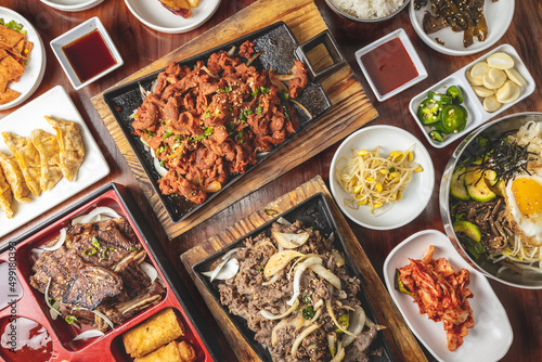 Принти на полотні Overhead Korean bulgogi barbecue flat lay view of a dinner feast with multiple bowls and platters of beef, pork, and side dishes