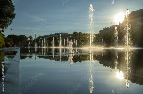 France, Nice, Famous place of Nice, square of fountain, mirror of water, playing kids, walking couples, a couple of old people are basking in the sunset, sun reflection, passing tram