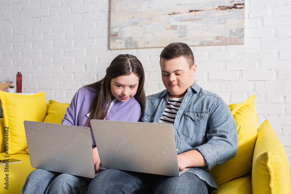 Teenagers with down syndrome using laptops on couch at home. Teenagers with down syndrome using laptops on couch at home.