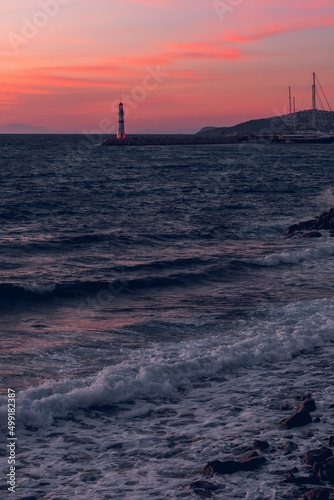 View of the lighthouse at sunset against the background of mountains. Aegean sea town in Turgutreis, Bodrum, Turkey. Sea surf at sunset. Sea breeze and salty fresh smell.