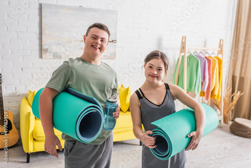 Cheerful teenagers with down syndrome holding fitness mats and sports bottle at home. photo