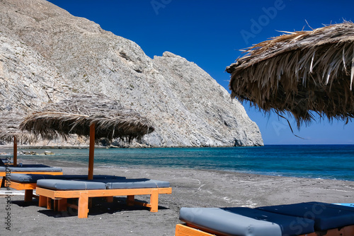 Sun beds and a sun umbrella at the famous black sandy beach of Perissa in Santorini