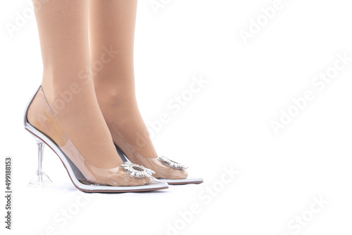 Women's legs in transparent shoes. White background. The shoes are embellished with rhinestones. Side view