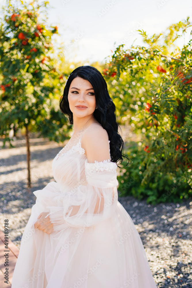 beautiful brunette bride in a wedding dress in a park with rowan trees. 