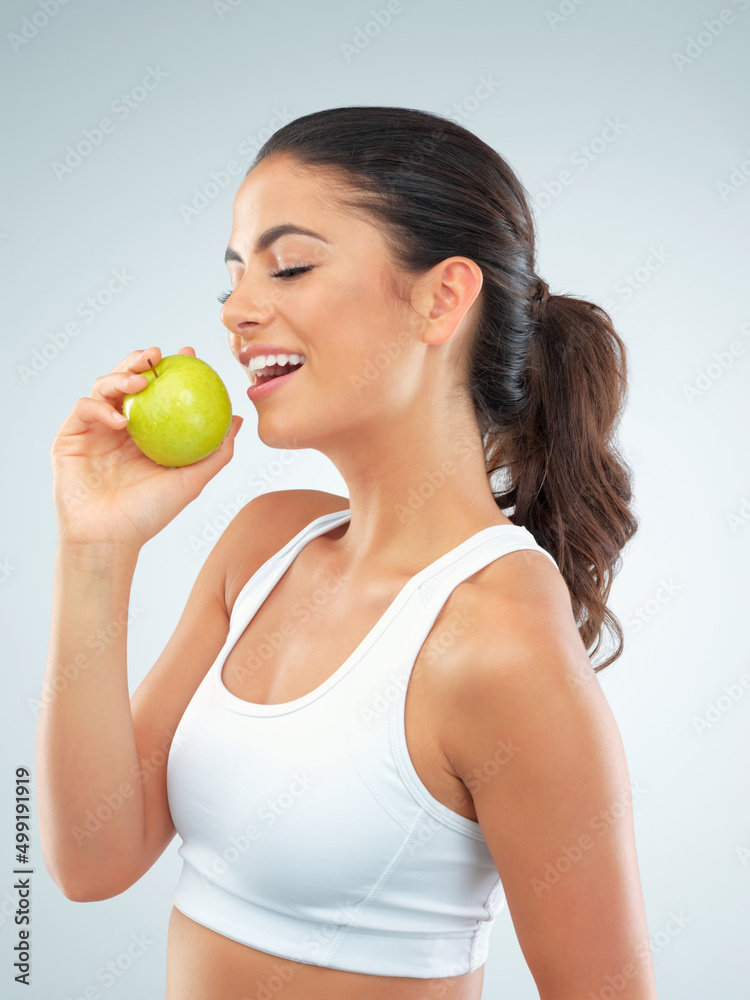 Healthy body, happy heart. Studio shot of a fit young woman eating an apple against a gray background. Healthy body, happy heart. Studio shot of a fit young woman eating an apple against a gray background.