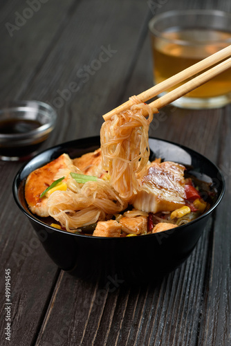 Asian rice noodles funchose with chicken, vegetables and sauce. Near chopsticks and green tea