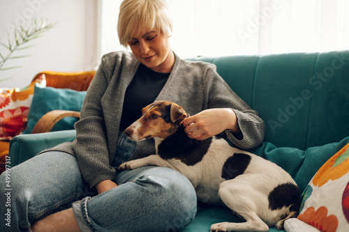 Woman cuddling and playing with her dog at home on the couch