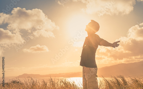 Foto It's a beautiful life! Young man with arms up to the sunlight standing in a meadow field