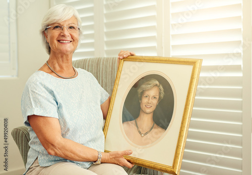 I havent changed a bit. Portrait of a happy senior woman posing with a portrait of herself at home. photo