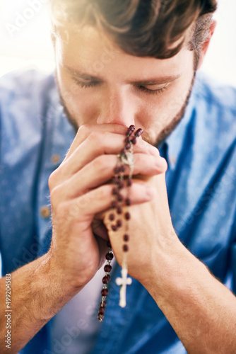 Putting his faith first. Cropped shot of a young man holding his rosary while praying.