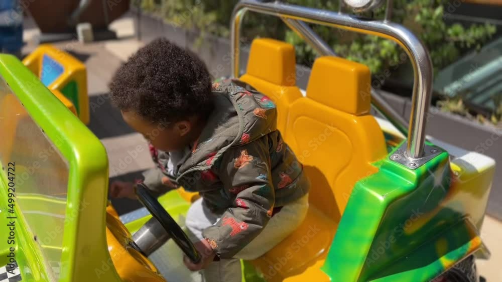 Two year old exotic afroeuropean child enjoying in a slot toy car, wearing a green jacket Two year old exotic afroeuropean child enjoying in a slot toy car, wearing a green jacket