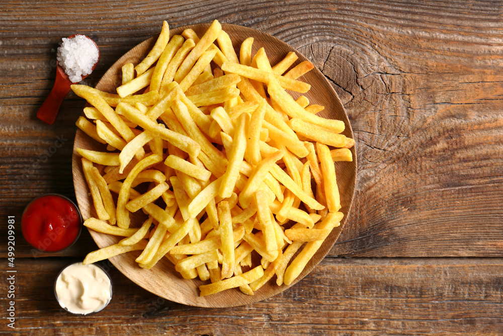 Plate with tasty french fries and sauces on wooden background