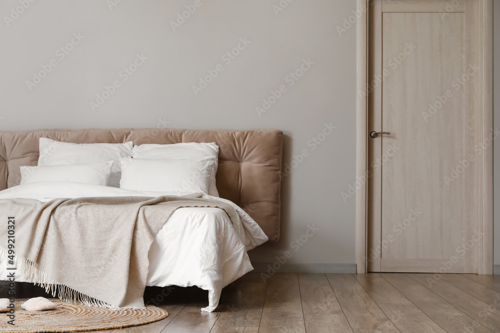 Comfortable bed and rug with slippers near light wall