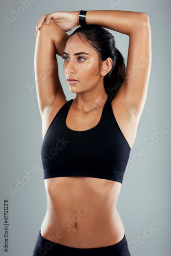Always remember to stretch before starting any exercise. Studio shot of an athletic young woman posing with her arms raised against a grey background.