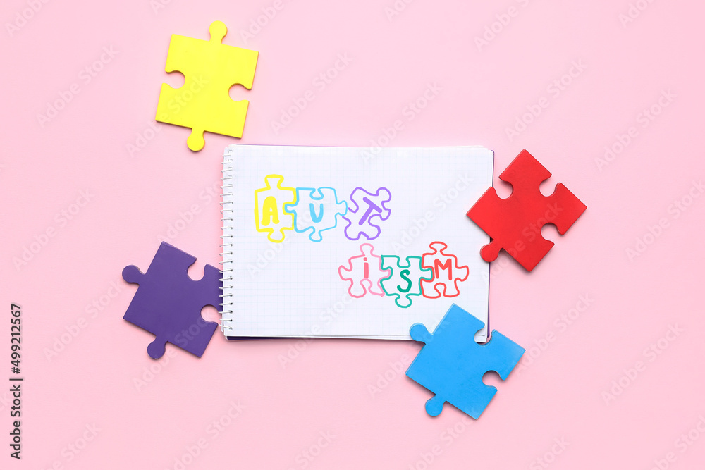 Notebook with word AUTISM and puzzle pieces on pink background Notebook with word AUTISM and puzzle pieces on pink background