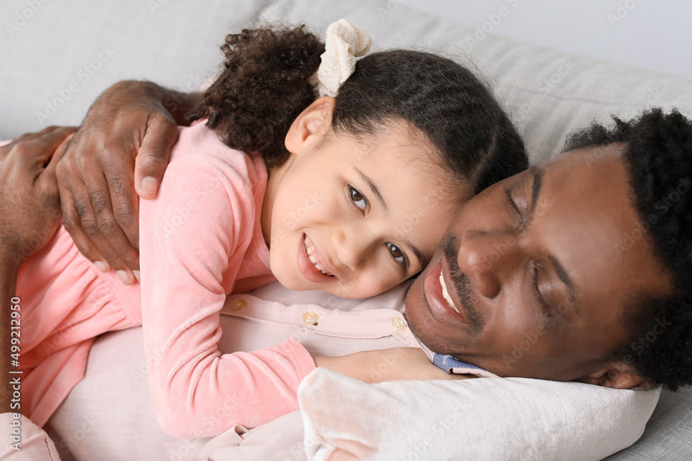 Happy African-American man and his little daughter lying on sofa at home Happy African-American man and his little daughter lying on sofa at home