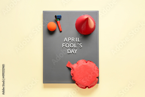 Grey board with text APRIL FOOL'S DAY, whoopee cushion and party set on yellow background photo