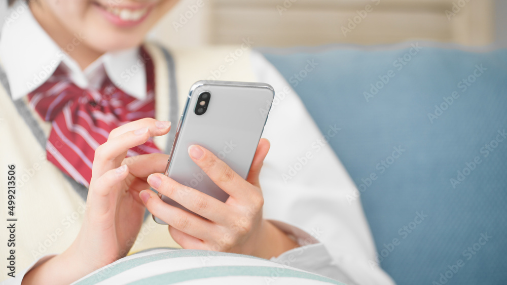 ソファーでスマートフォンを操作する女子高生 ソファーでスマートフォンを操作する女子高生