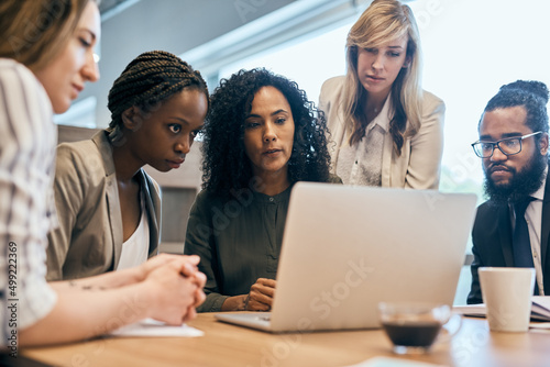 You guys need to take a look at this. Shot of a group of focussed businesspeople browsing on a laptop together in the office at work during the day.