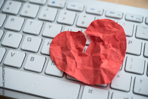 Red broken heart paper on white keyboard computer background. Online internet romance scam or swindler in website application dating concept. Love is bait or victim.