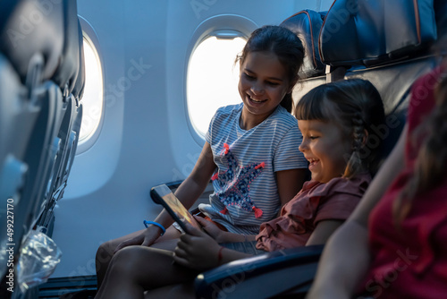 Adorable little girls travel by plane. Cute Kids sit at the window of an airplane and use a digital tablet during the flight. Family Traveling abroad with children