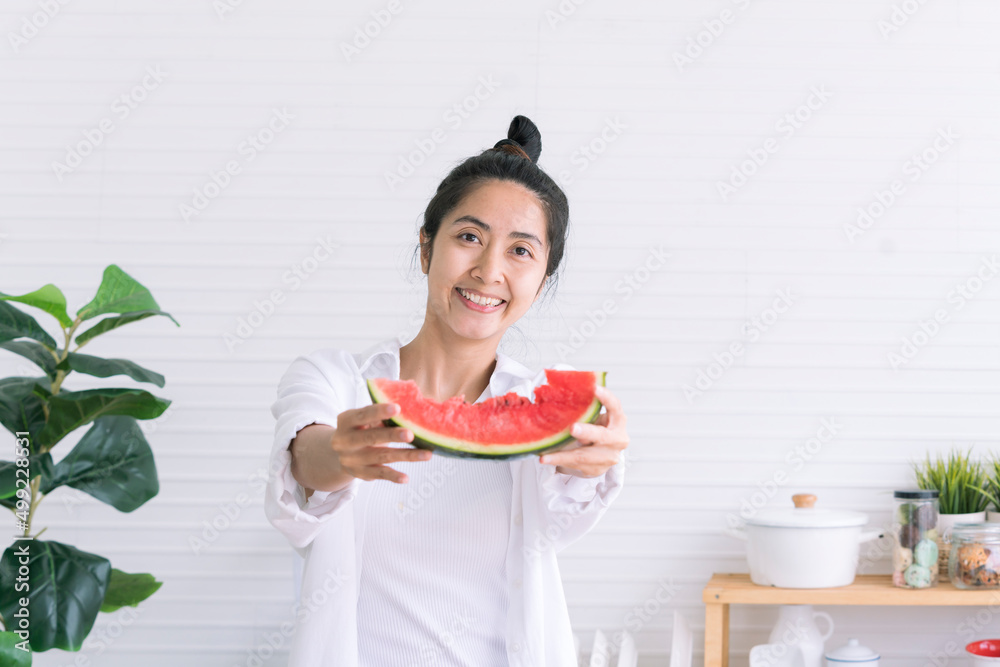 Asian woman showing bitten red watermelon in kitchen. Asian woman holding watermelon in the kitchen. Woman eating fresh watermelon while standing in the kitchen. Asian woman showing bitten red watermelon in kitchen. Asian woman holding watermelon in the kitchen. Woman eating fresh watermelon while standing in the kitchen.