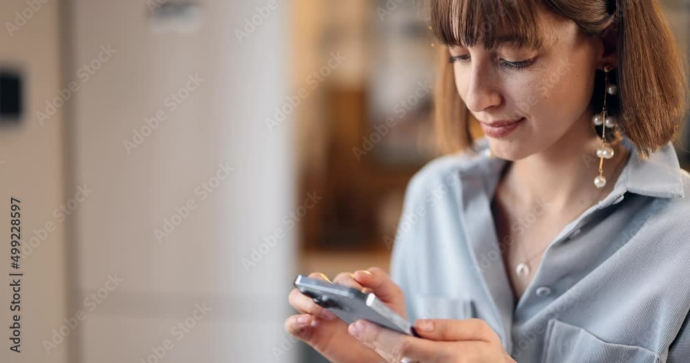 Thoughtful woman using phone at home, close-up view. Caucasian brunette girl surfing internet on smartphone