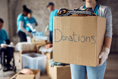 Photographie Close up of woman holds cardboard box filled with donated clothes while volunteering at charity center