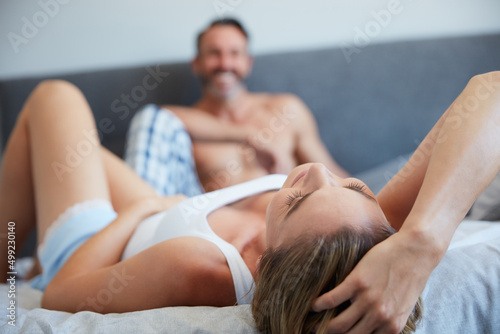 Sharing a bed with happiness. Shot of a young woman lying on a bed with her husband in the background.