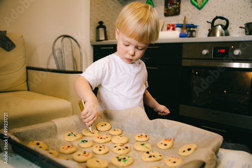 A little blond boy of two years old is cooking homemade cookies in the kitchen