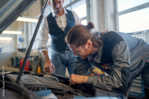 Man with car mechanic in auto service looking at a car motor