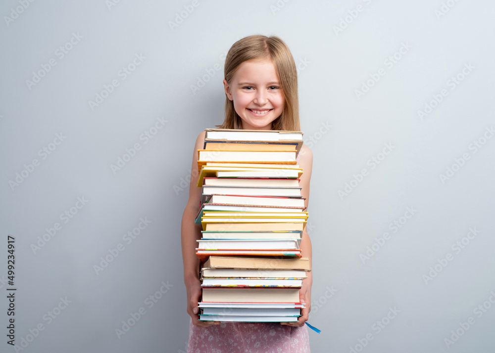 Primary school girl holding stack of books on a grey wall background Primary school girl holding stack of books on a grey wall background